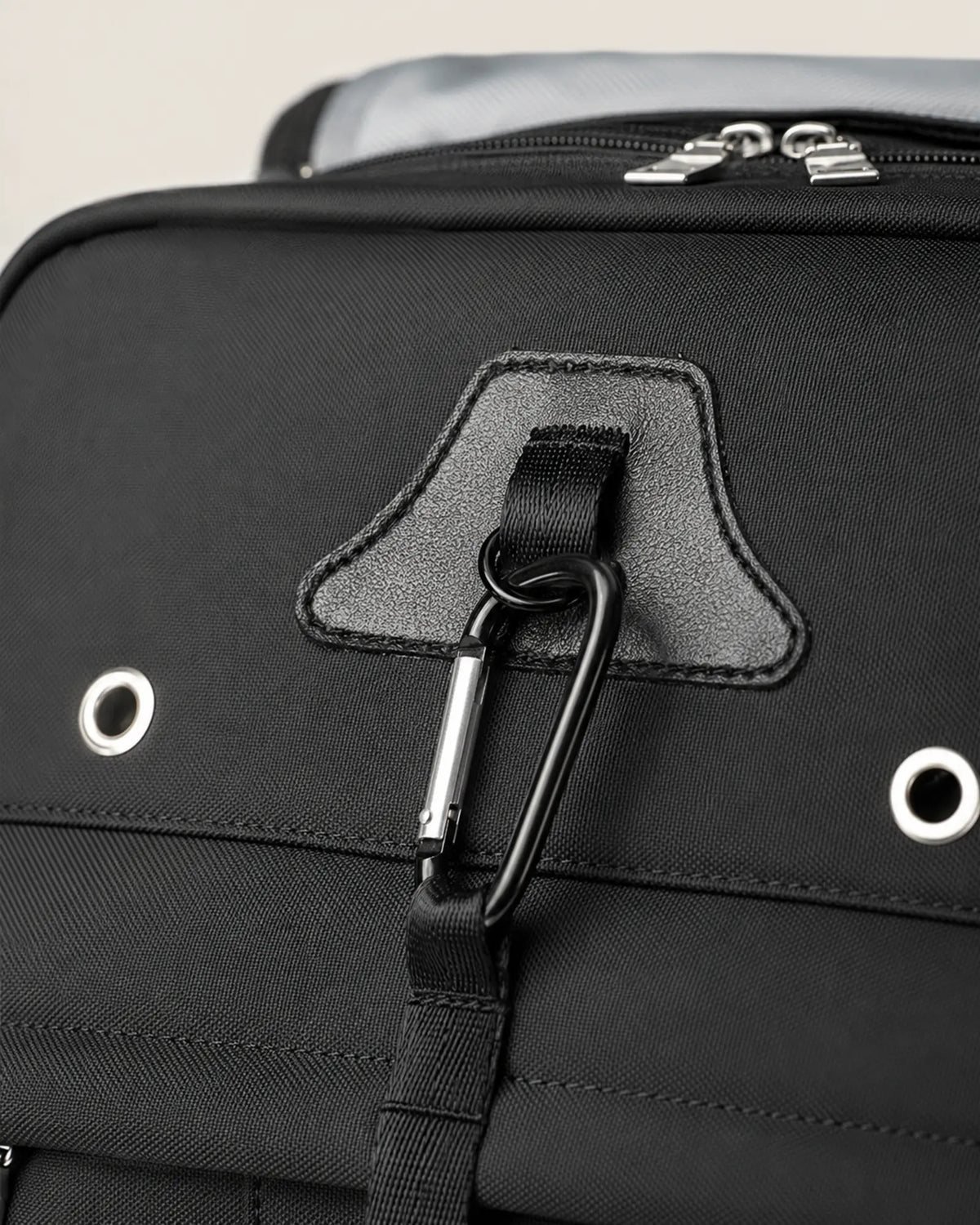 Close-up of the carabiner and reinforced front webbing on a black travel backpack