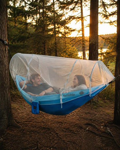 Two campers using the blue double hammock under its mosquito net in a forest