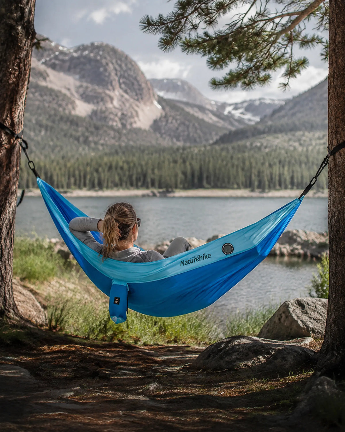 Traveler relaxing in the blue camping hammock beside a mountain lake