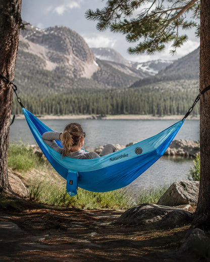 Traveler relaxing in the blue camping hammock beside a mountain lake