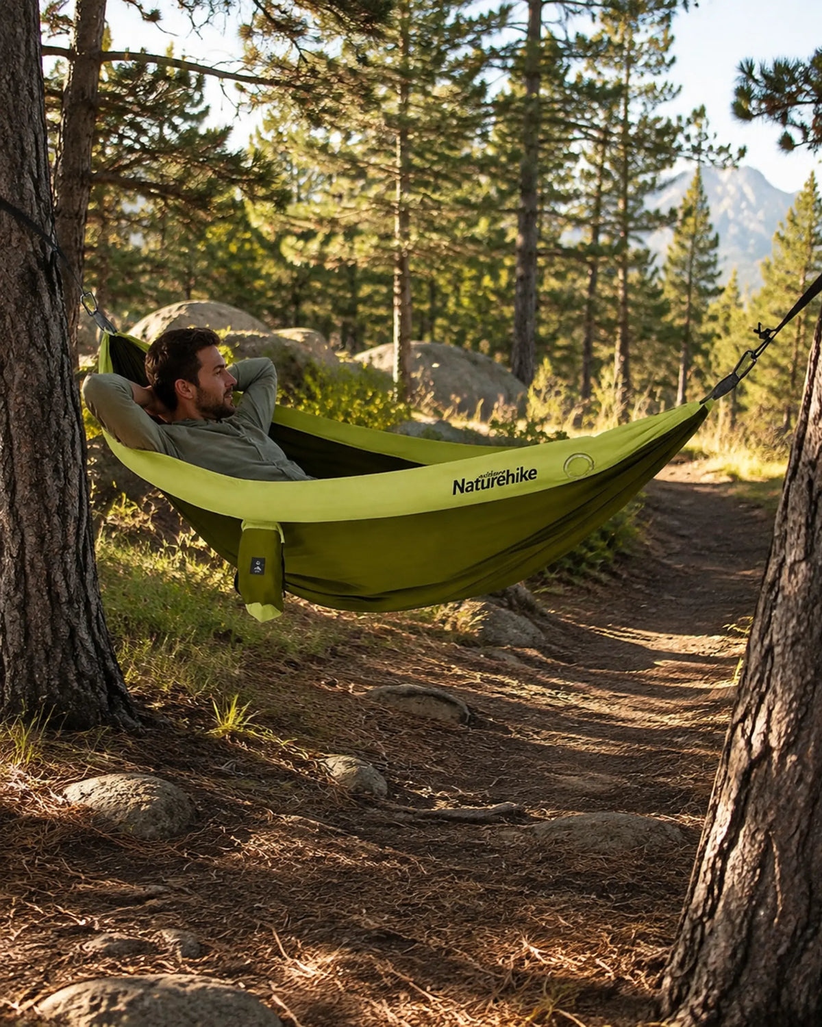 Hiker relaxing in the green double camping hammock beside a forest trail