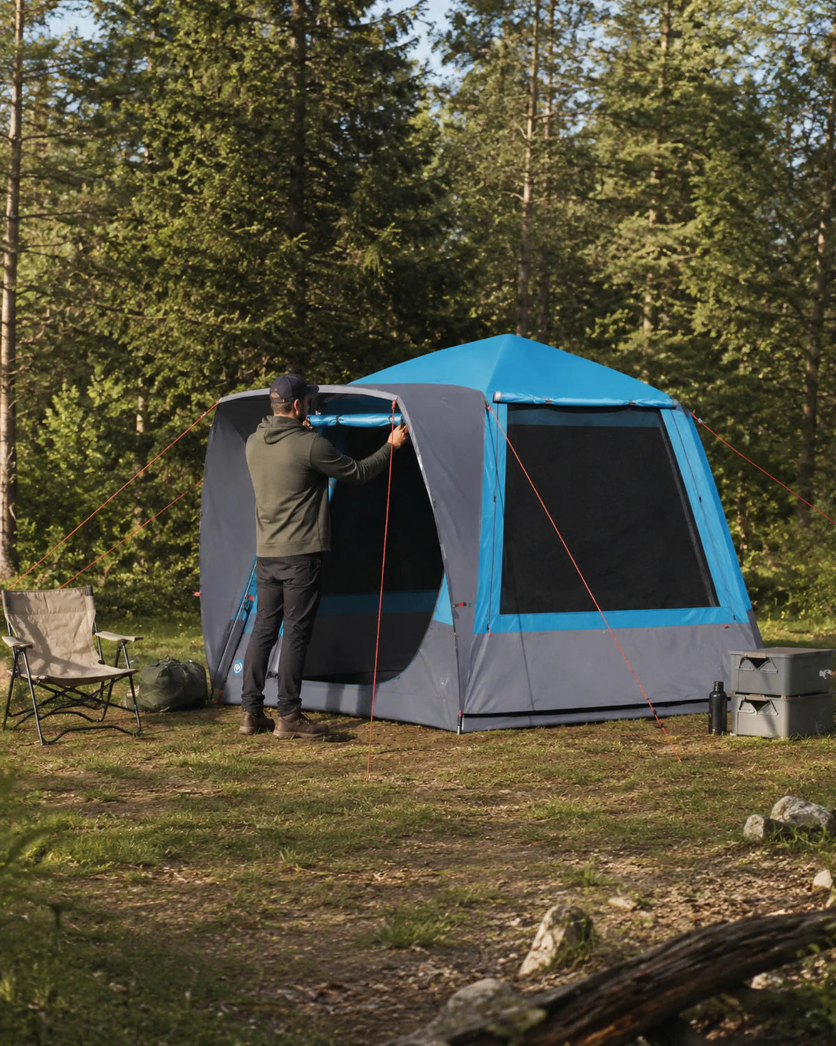 Camper adjusting the blue large family tent at a forest campsite