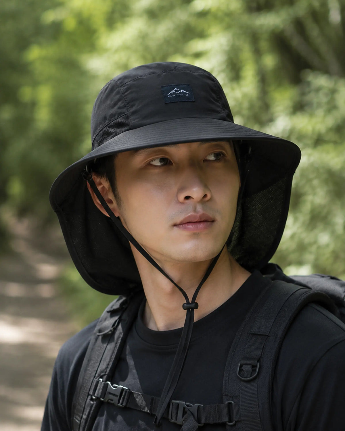 Hiker wearing black wide-brim sun hat with mesh neck protection on forest trail