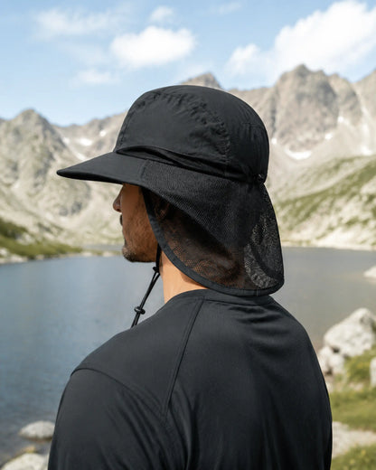 Hiker wearing black neck-flap sun hat beside an alpine lake