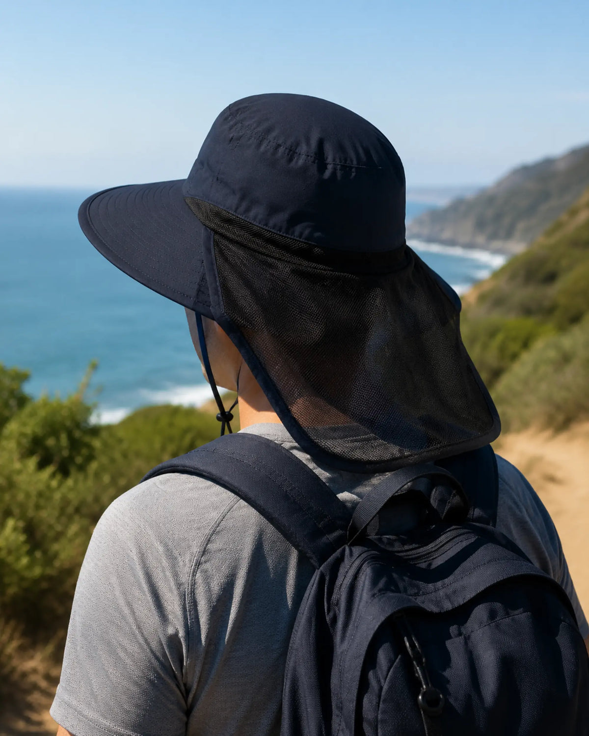 Hiker wearing dark blue neck-flap sun hat on a sunny coastal trail