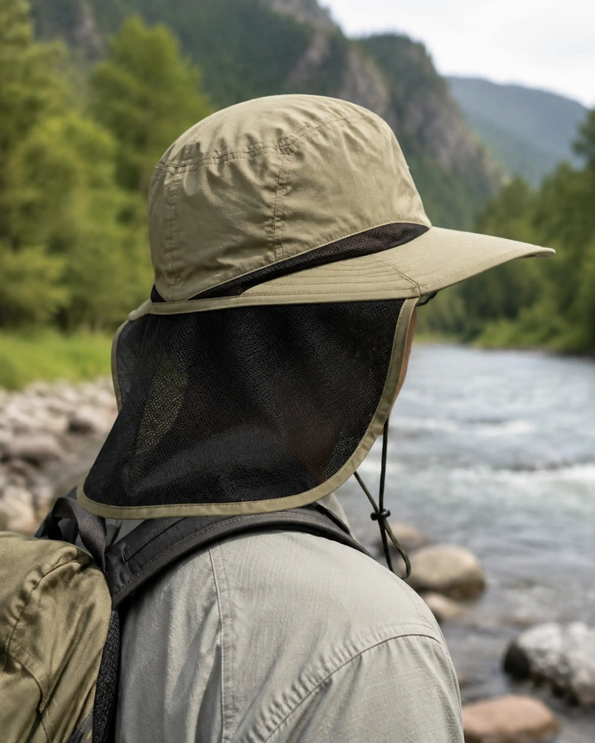 Hiker wearing green neck-flap sun hat beside a riverside trail