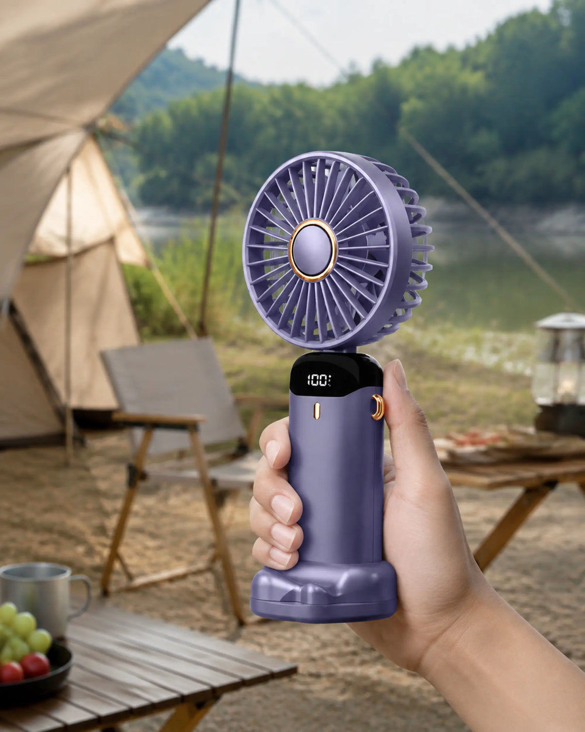 Blue handheld portable fan used naturally at a shaded lakeside campsite