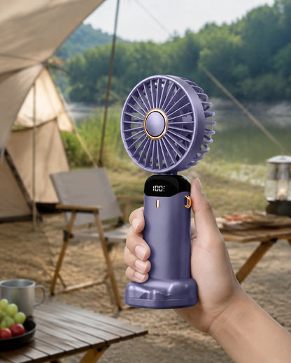 Blue handheld portable fan used naturally at a shaded lakeside campsite