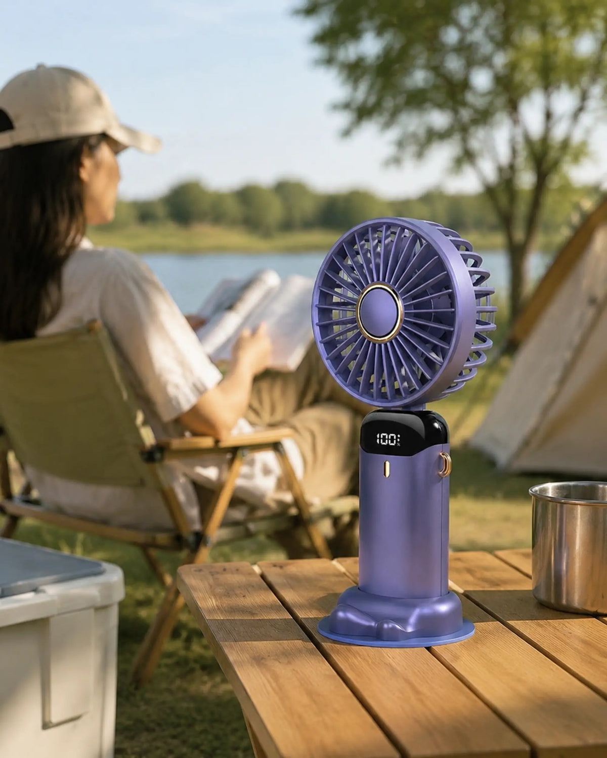 Blue portable fan cooling a reader at a warm lakeside campsite