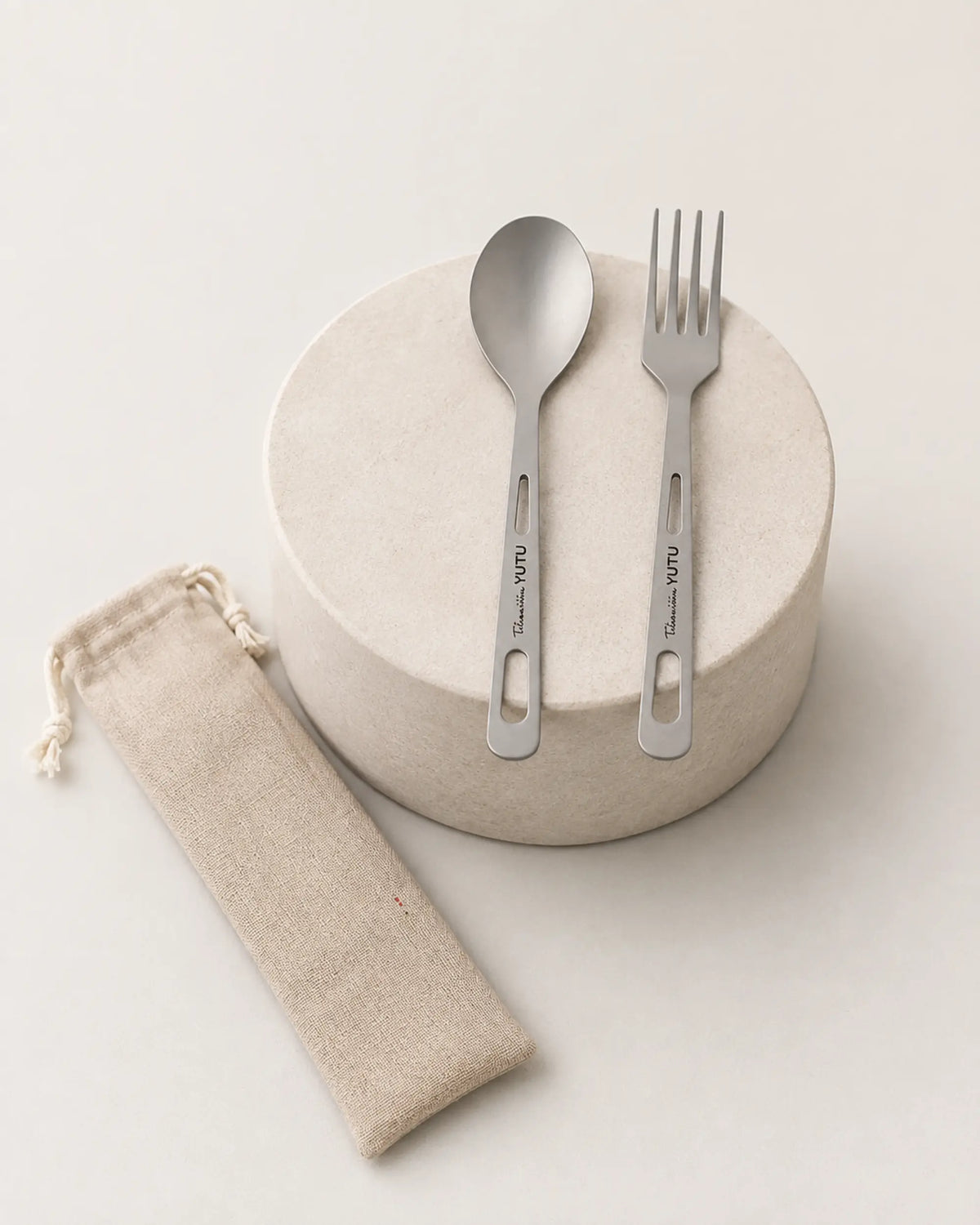 ARWE two-piece titanium cutlery displayed on a minimalist stone pedestal