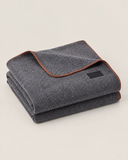 Folded light grey wool-blend camping blanket with orange locking-stitch edges in a front three-quarter view