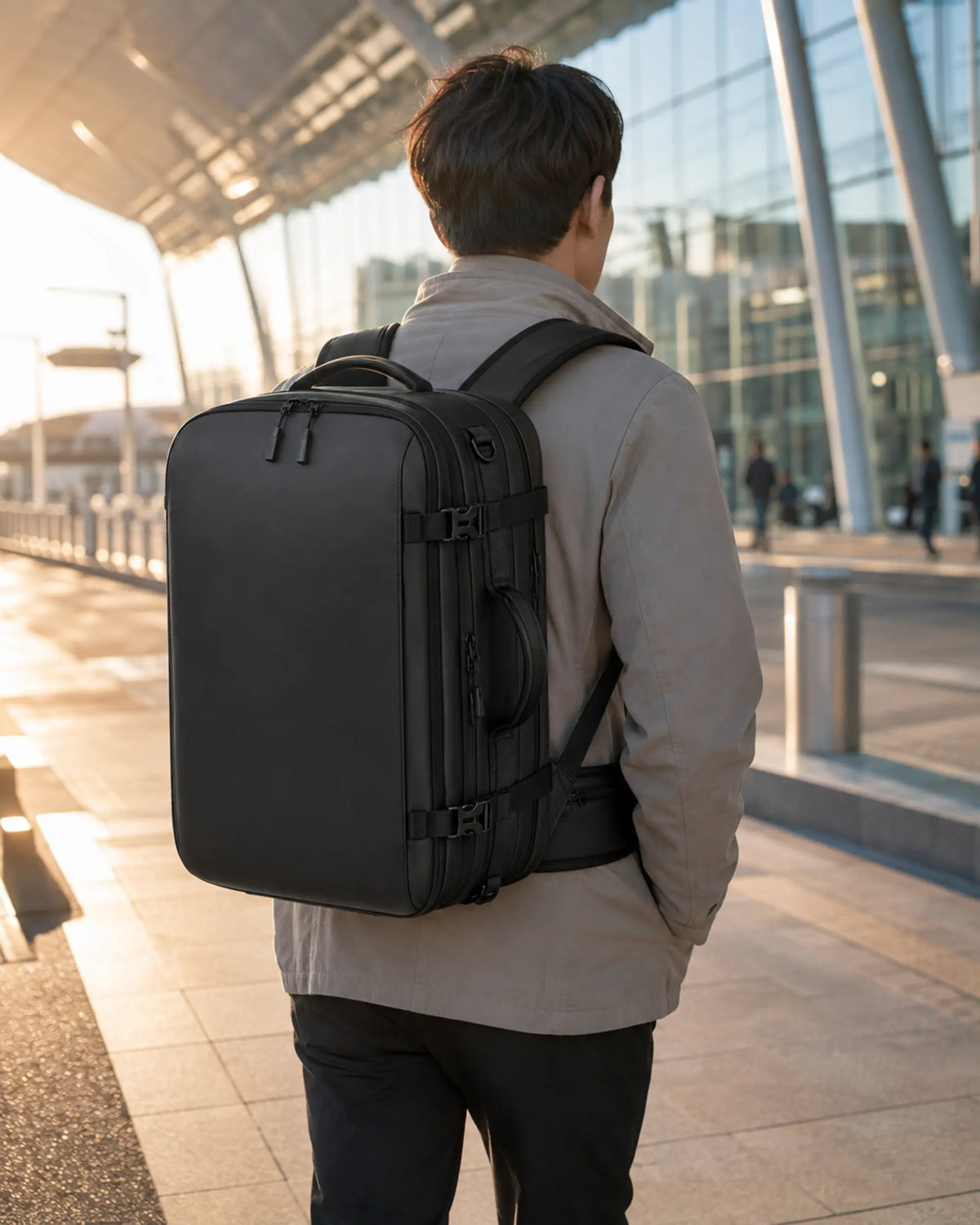 Black business travel backpack worn by a traveler outside a modern airport terminal