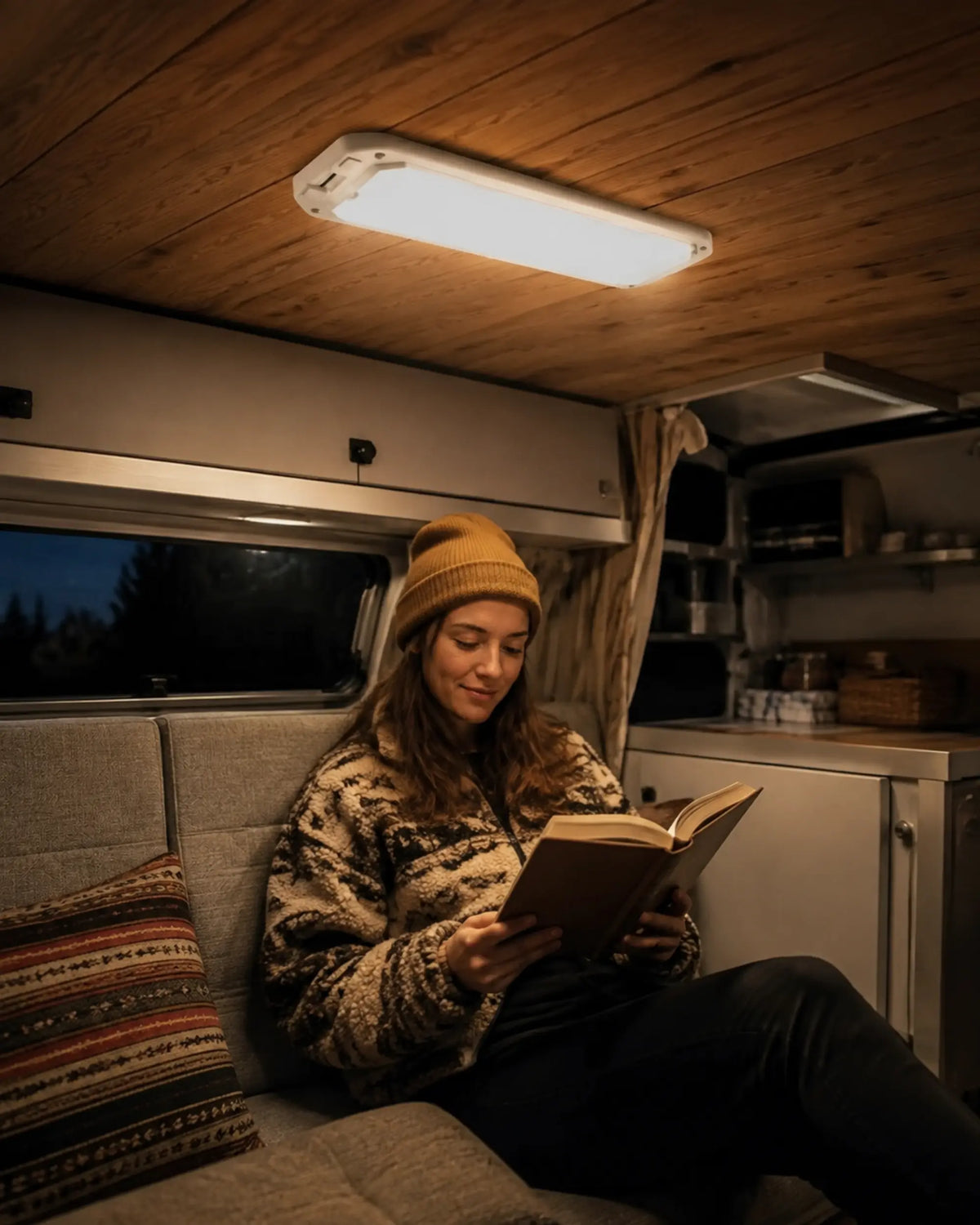 Warm RV ceiling light illuminating a traveler reading inside a camper at night