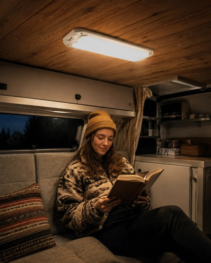 Warm RV ceiling light illuminating a traveler reading inside a camper at night